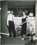Carroll Gartin standing with [wife] by fireplace by Author Unknown