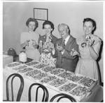 Walter H. (Skeet) Hunt with three unidentified women standing behind shrimp table. by Author Unknown