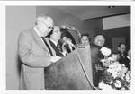 Eastland standing behind a podium at the 1978 Symposium of Deposit Guaranty National Bank with unidentified men in the background. by Author Unknown