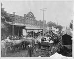 Crowded street scene with oxen and wagons in front of D.L. Brown Hardware store. by W. W. McMillan