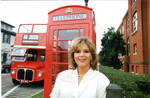 Woman posing in front of phone box and double decker tour bus. by Author Unknown