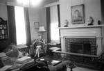 Library at Rowan Oak with unidentified woman sitting in chair by Edwin E. Meek