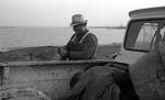 White man next to pickup truck near the water by Edwin E. Meek