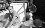 White man sitting on back of truck next to large cooler and scale by Edwin E. Meek