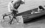 Man pushing small boat onto the water by Edwin E. Meek