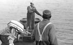 African American man looks on as white man pushes off in a boat by Edwin E. Meek