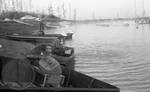 White man sitting in flooded boat with other boats, man, and car in background at Hurricane Landing by Edwin E. Meek