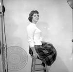 Unidentified young woman sitting on stool in plaid skirt by Edwin E. Meek