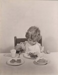 Young blond child eating with a glass of milk. by USDA