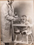 Adult female administering Cod Liver Oil to an infant in a high chair. by USDA