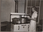 Cafeteria worker ladling food into bowls from a large pot. by USDA