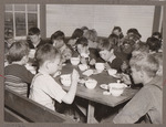 Children eating school lunch in a cafeteria filled with trestle tables. by USDA