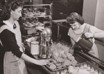 Betty Lehman (left) operates the mechanical juicer, while Patsy McElroy pours the orange juice into glasses at Hyattsville, Md., High School. Both are home economics majors and get credit for working in the lunchroom which serves about 750 students daily under the joint Federal-State School Lunch Program.