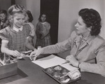 Two mothers work as volunteer "checkers" at East Silver Spring, Md., Elementary School. Here Mrs. Marion Dieste takes the money from her daughter, Judith, who is having the regular Type "A" lunch. Mrs. Dieste keeps track of the various types of lunches the children buy, jotting down the information on a record sheet. by USDA