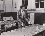 Putting a half-pint of whole milk at each place, Mrs. Matthew Luciani, a volunteer, gets ready for the long line of hungry children. Mrs. Luciani heads the hard-working hot lunch committee of the Parent-Teachers Association. Center School, Bethel, Conn. NSL Program. by USDA