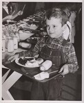 First grader Robert McDaniel comes down the line with his hot, nutritious lunch consisting of mashed potatoes with gravy, roast beef, a roll and butter, milk, prunes, and a sugarcoated cookie. by USDA