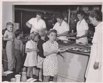 Children accompanied by their teachers enter cafeteria by grades and secure plates of food served from steam table. Dr. Hathaway (at far right) is taking sample plates, selected at random, as they are prepared for children, to be checked for nutritive value by chemical analysis. An average sized serving of each food is determined by averaging the weights of five samples in this way. School lunch study by U. S. Bureau of Human Nutrition and Home Economics Cumberland, Maryland by USDA