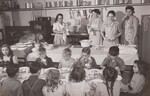 Children at the Liberty Township Consolidated School near Port Allegany, McKean County, Pa., with a group from the Brooklyn School, a rural school 2 miles away, enjoy a hot nutritious lunch served, under the Federal-State school lunch program, around tables seating 50 to 75 children, in the school basement. Mrs. Edith Cordell (left), a trained dietitian, directs the program. Mothers of the pupils take turns assisting her in preparing and serving the lunches. by USDA