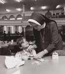 Sister Marie Patrice helps student at St. Anthony de Padua Parochial School, during lunch. This school recently converted from cup can to in flight type lunches. U.S. Department of Agriculture's Food and Nutrition Service is charged with the responsibility of the School Lunch Program. Philadelphia, Pennsylvania.